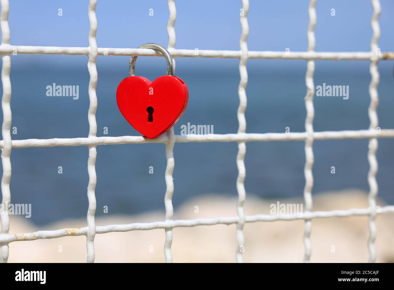 Red heart padlock on fence in front of blue sea, symbol of eternal love Stock Photo
