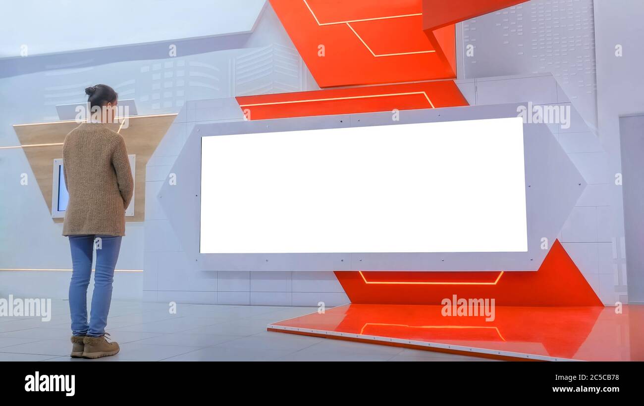 Woman looking at blank large wide interactive wall white display at modern technology exhibition or museum with futuristic sci-fi interior. Mock up Stock Photo