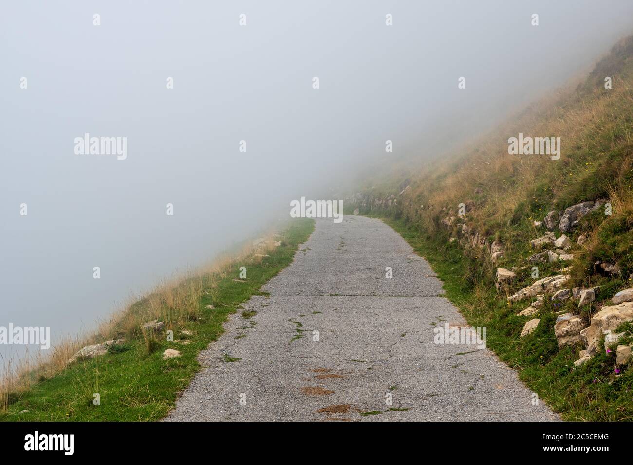 Narrow mountain asphalt road fading in the fog. Misty and foggy Alpine road, Lombardy, Italy. Stock Photo