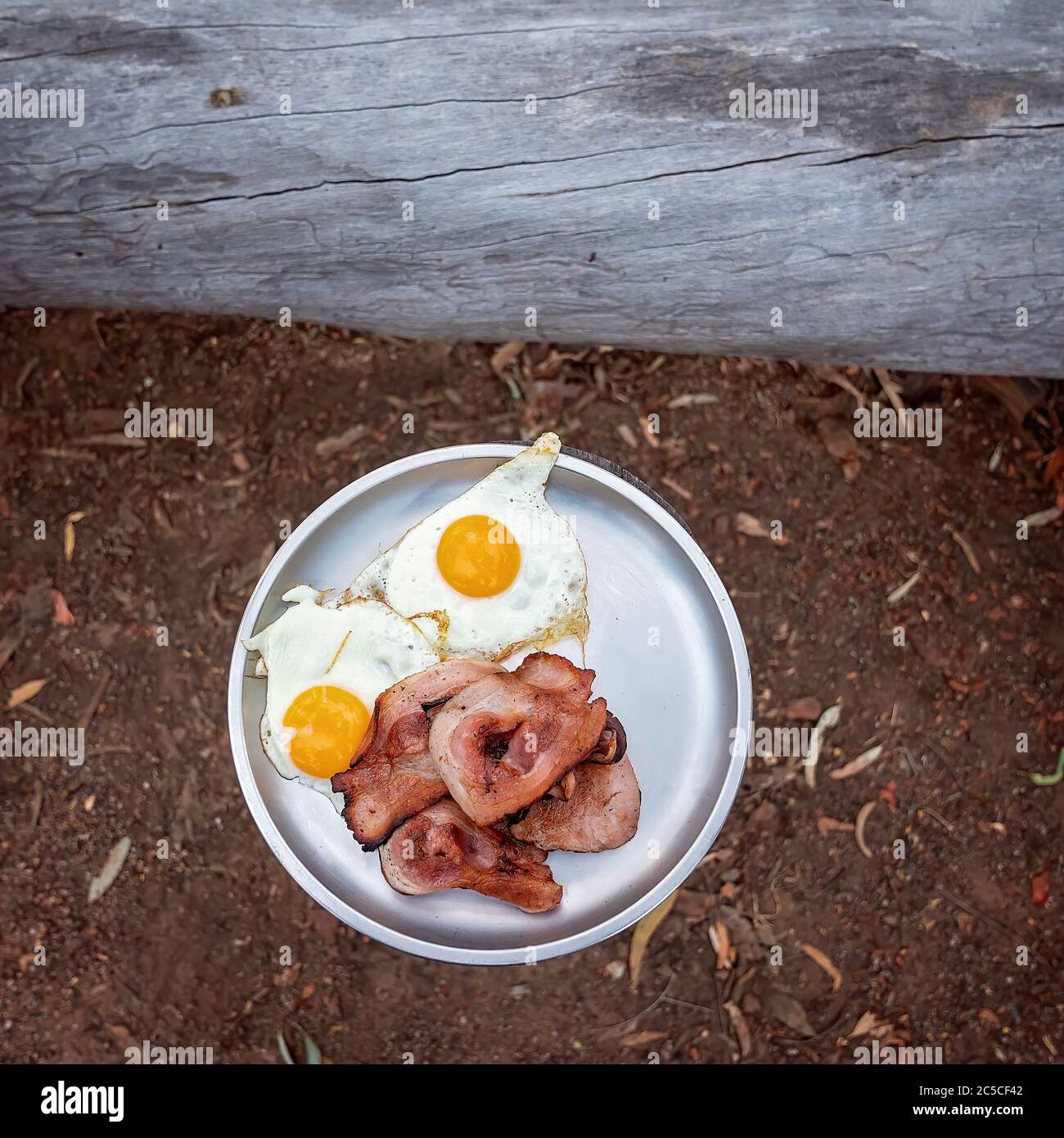 Bacon and eggs served on a tin plate at a campfire bush breakfast on an Australian outback tourist resort Stock Photo