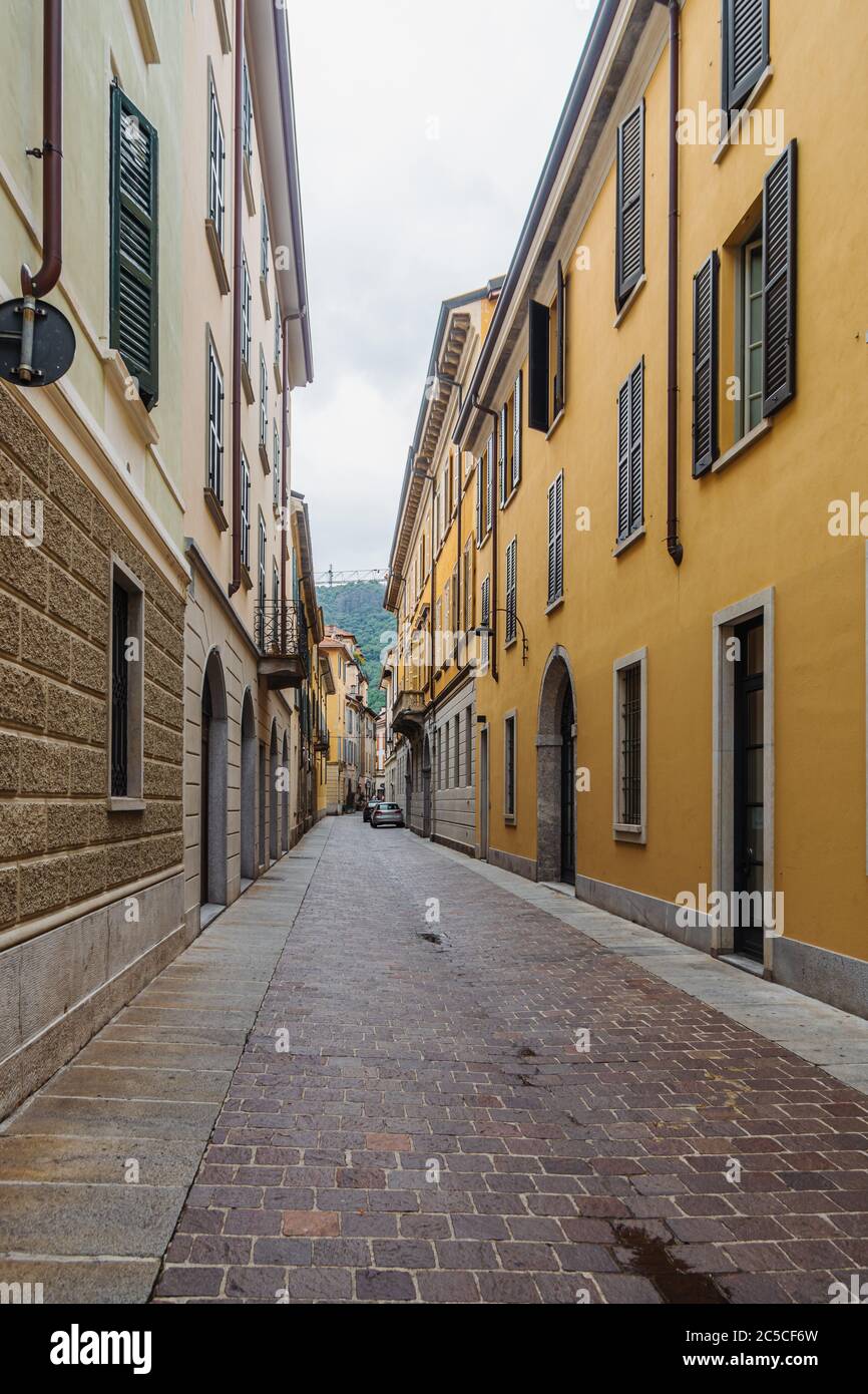 View of a narrow, empty street with pastel colorful facades of houses in Como, Italy. Stock Photo