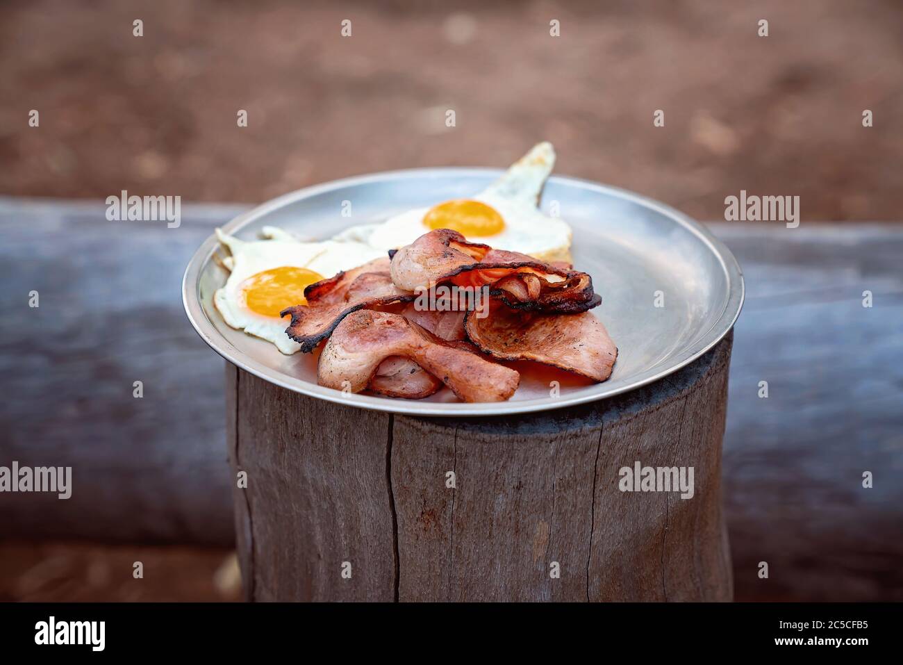 Bacon and eggs served on a tin plate at a campfire bush breakfast on an Australian outback tourist resort Stock Photo