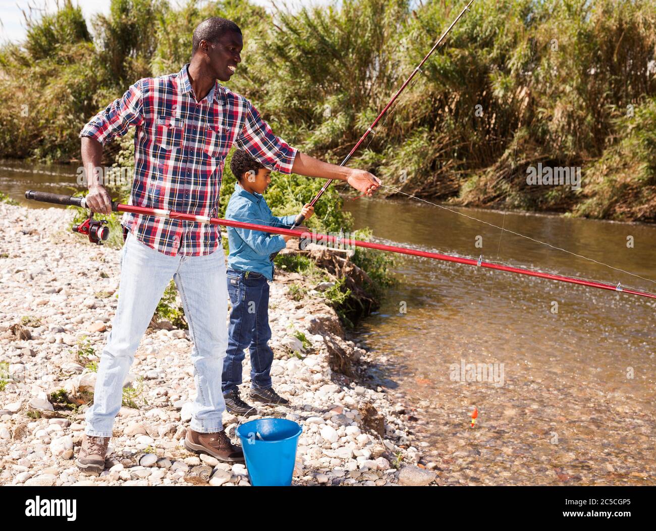 Portrait of fishermen - African boy and his father fishing with rods on river Stock Photo