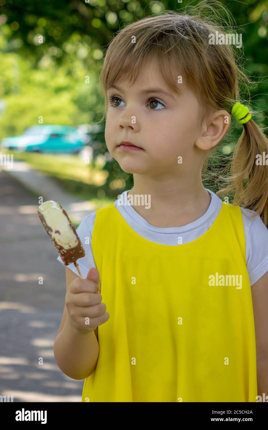 A Little Girl In A Yellow Dress Licking Ice Cream In Nature Stock Photo 
