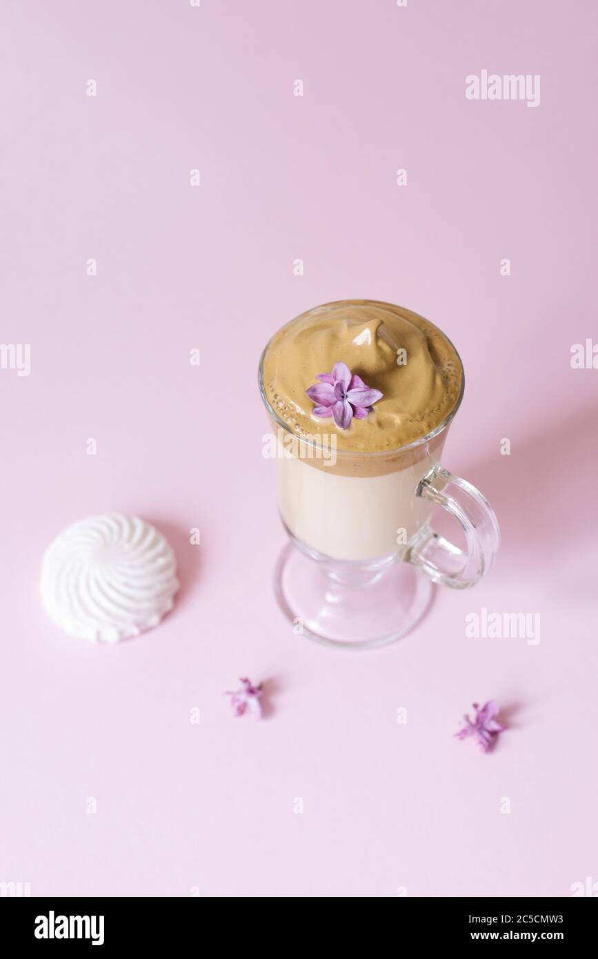 Beautiful dalgon coffee drink. Coffee mug in clear glass with foam and lilac flower on a lilac background. Sweetness to the drink-marshmallow Stock Photo