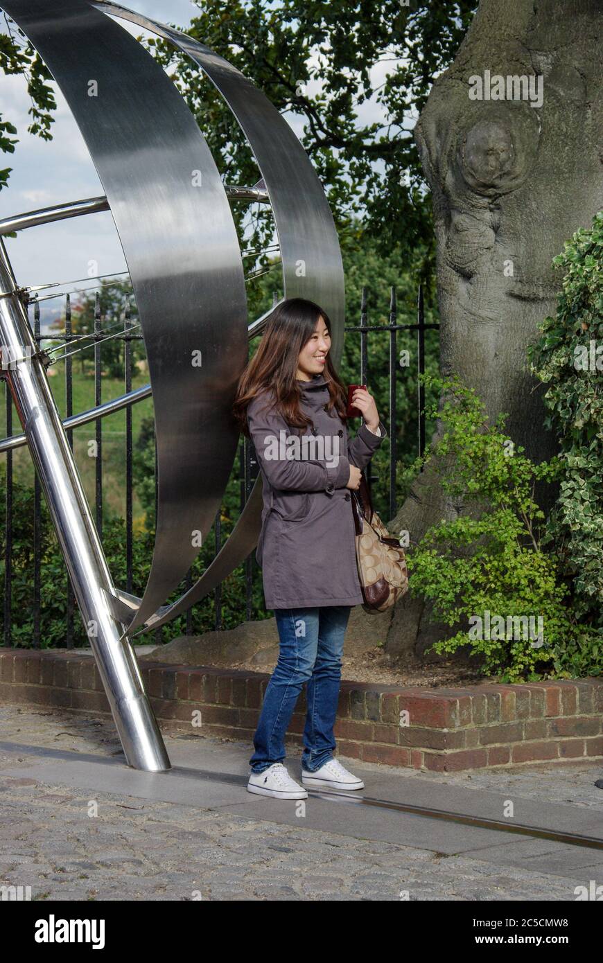 Japanese tourist poses for a photo standing astride the Meridian Line, Royal Observatory, Greenwich, London Stock Photo