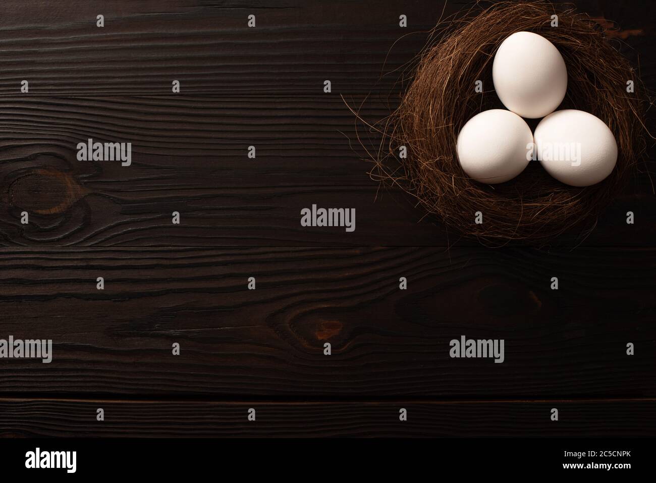 top view of white chicken eggs in brown nest on dark wooden background ...