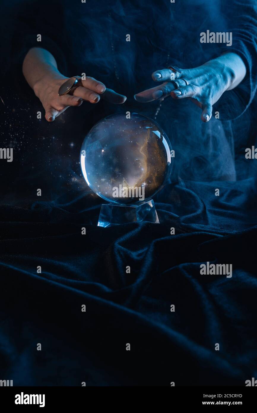 Cropped view of witch performing ritual with crystal ball on dark blue Stock Photo