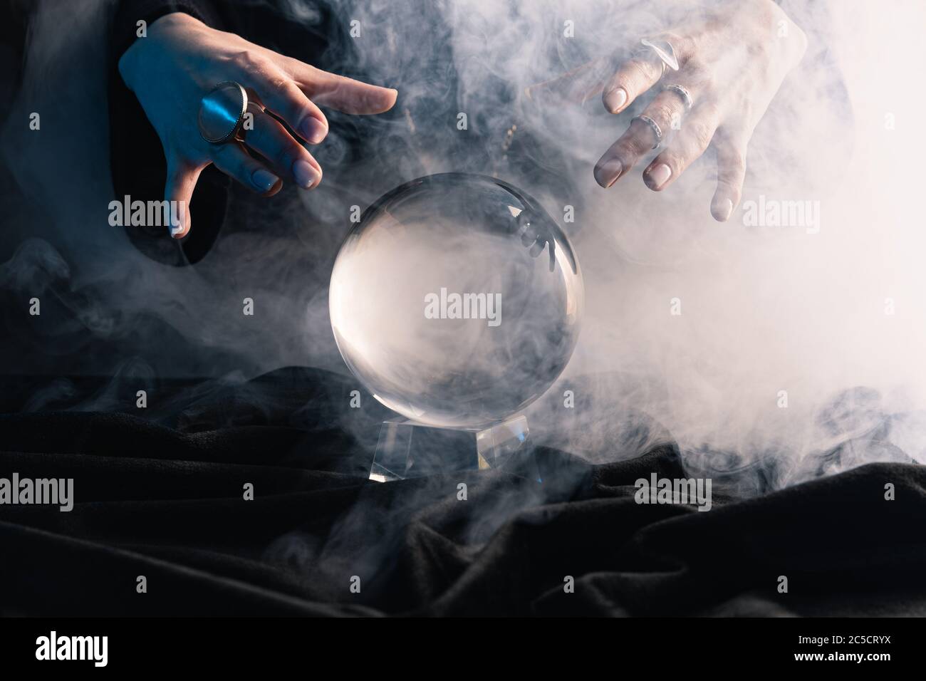 Cropped view of female hands above crystal ball with smoke on dark Stock Photo
