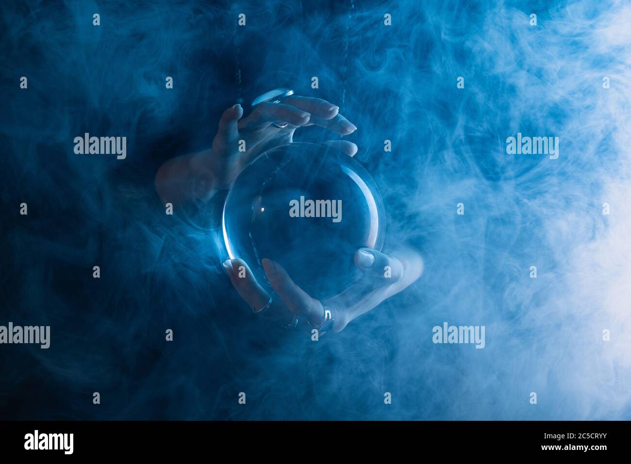 Partial view of witch holding crystal ball with smoke around on dark blue Stock Photo