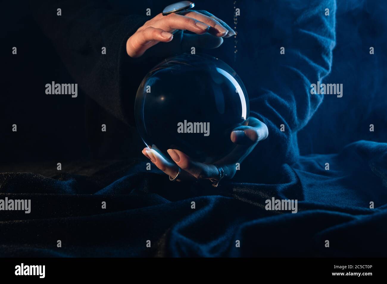 Partial view of witch with crystal ball on dark blue Stock Photo