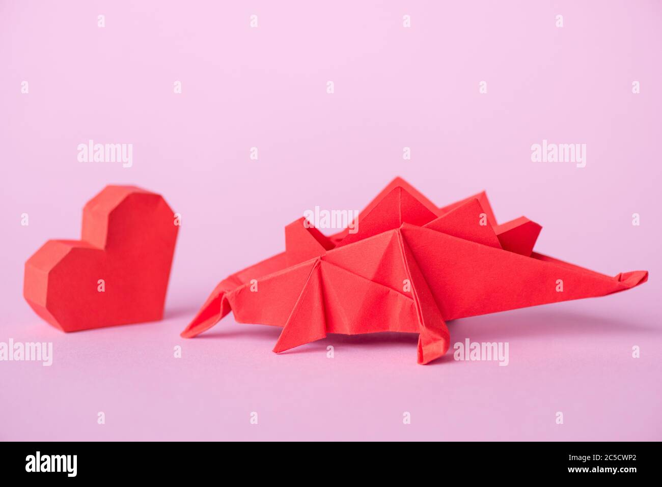 red paper heart near origami dinosaur on pink Stock Photo
