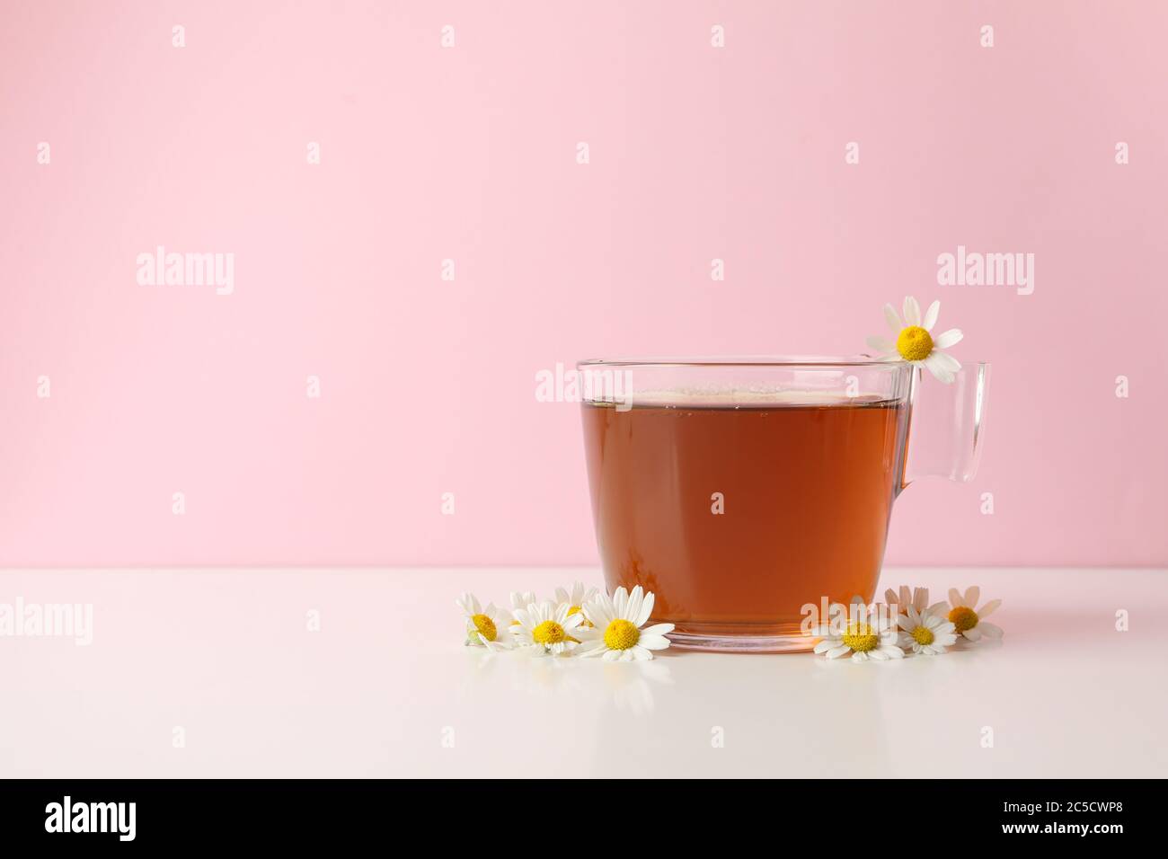 Cup of tea and chamomile on white table against pink background Stock ...