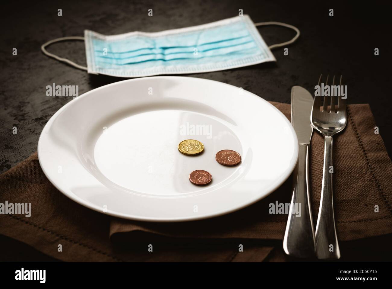 Euro cents coins on white empty plate and medical mask on black background. Lack of money during quarantine, poverty and unemployment concept Stock Photo
