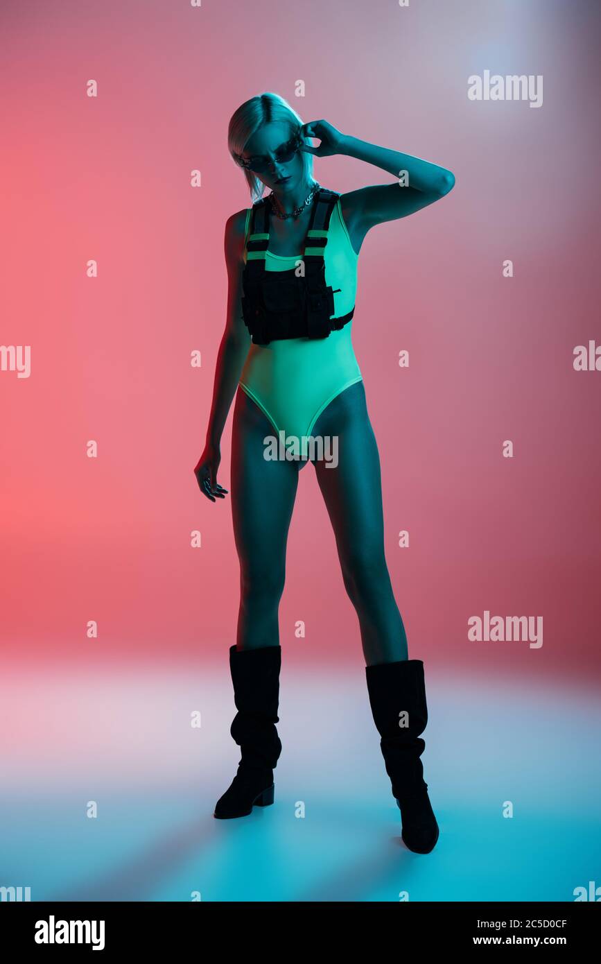 model in futuristic leotard and fire-shaped sunglasses posing on pink in blue light Stock Photo