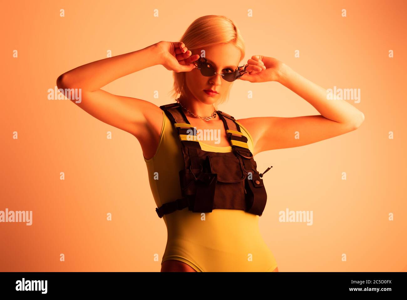 fashionable futuristic young woman posing in fire-shaped sunglasses on orange Stock Photo