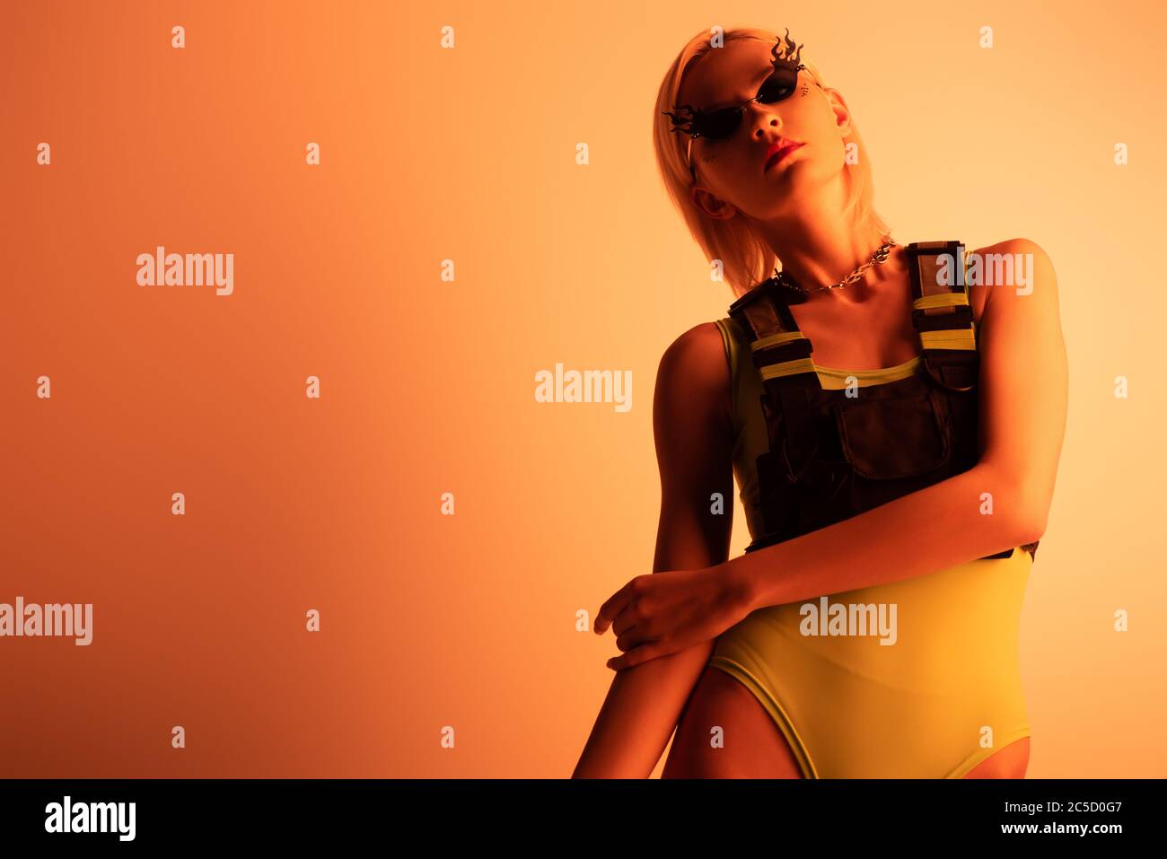 fashionable attractive futuristic girl posing in fire-shaped sunglasses on orange Stock Photo
