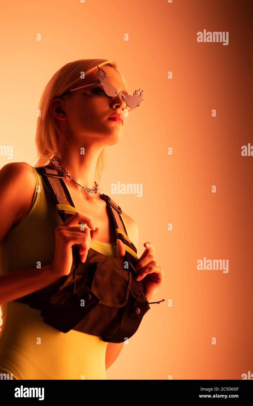 attractive stylish futuristic girl posing in fire-shaped sunglasses on orange Stock Photo