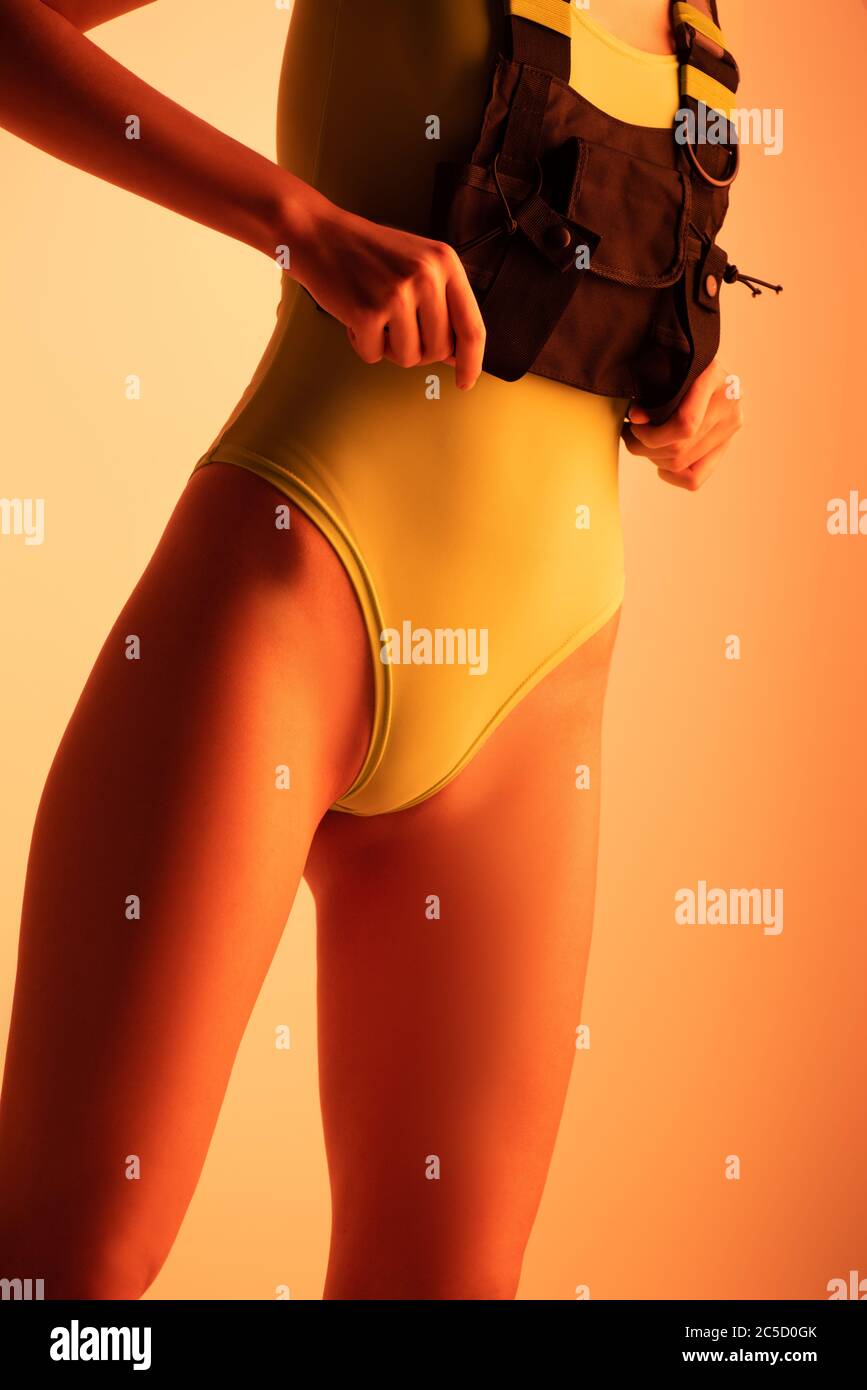 cropped view of fashionable futuristic girl posing in yellow bodysuit on orange Stock Photo