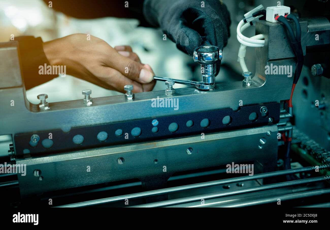 Mechanic technician hand fixing industrial machinery in factory. Professional technician service and maintenance packing machine equipment. Worker use Stock Photo