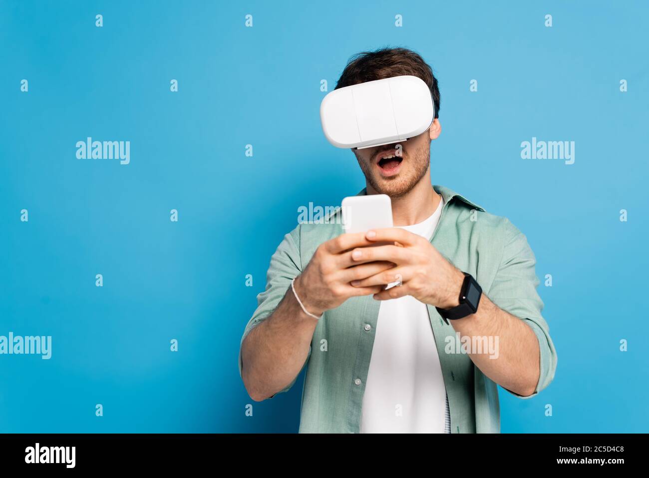 shocked young man in vr headset using smartphone on blue Stock Photo