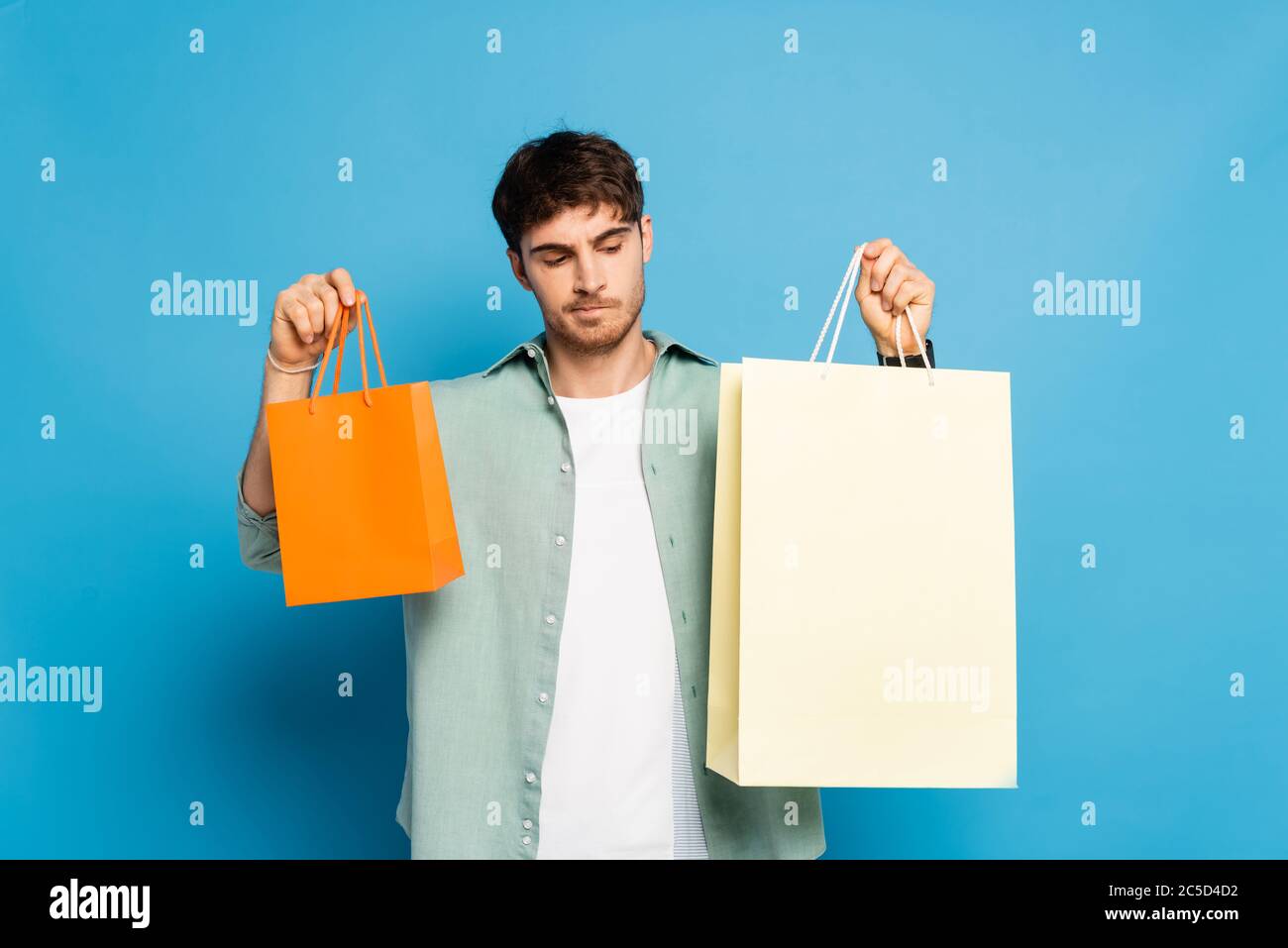 thoughtful young man holding shopping bags on blue Stock Photo