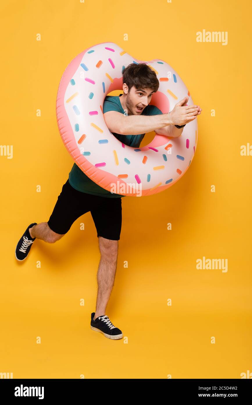 funny young man jumping into inflatable donut on yellow Stock Photo