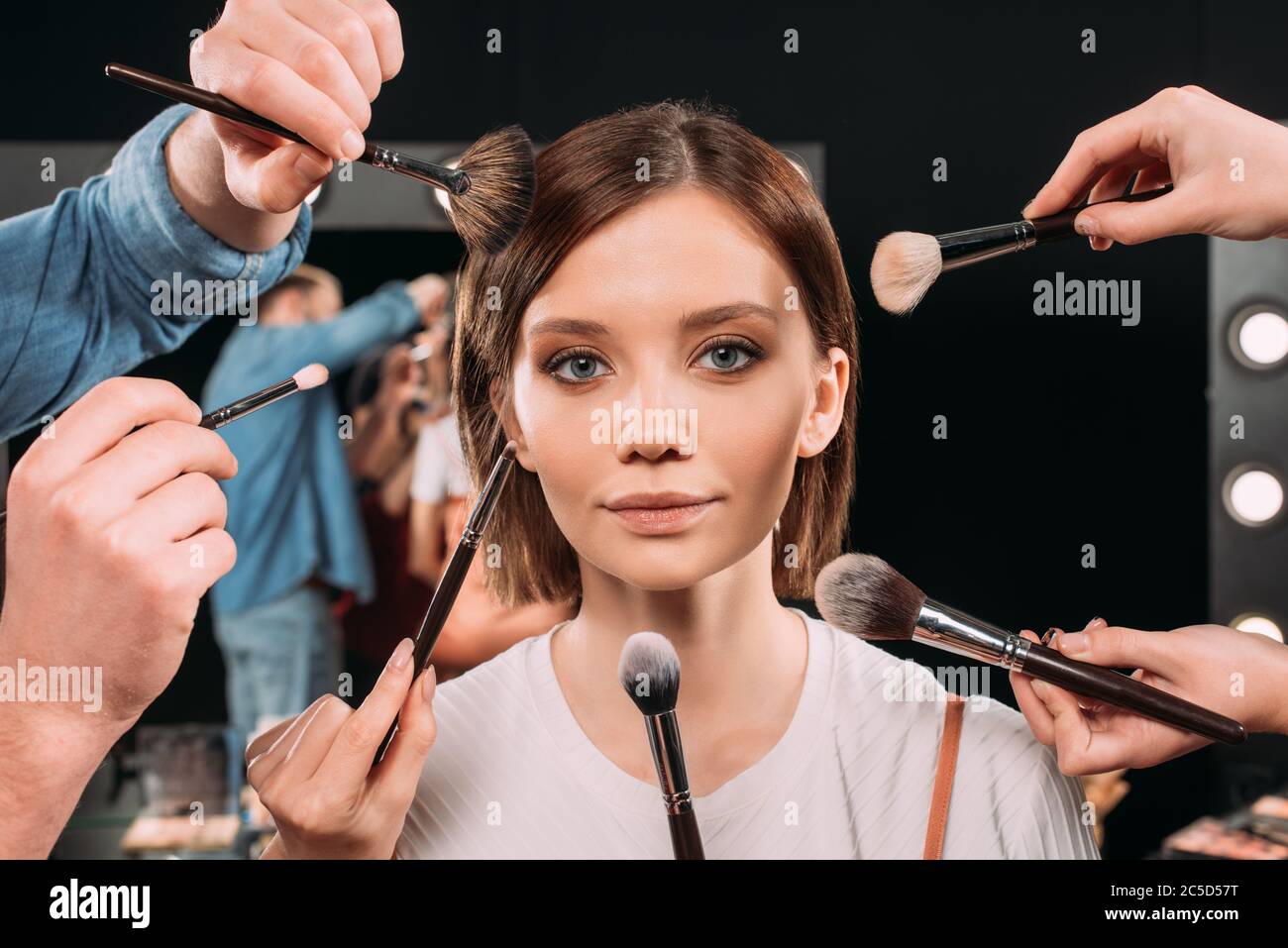 Makeup artists holding cosmetic brushes near beautiful model in photo
