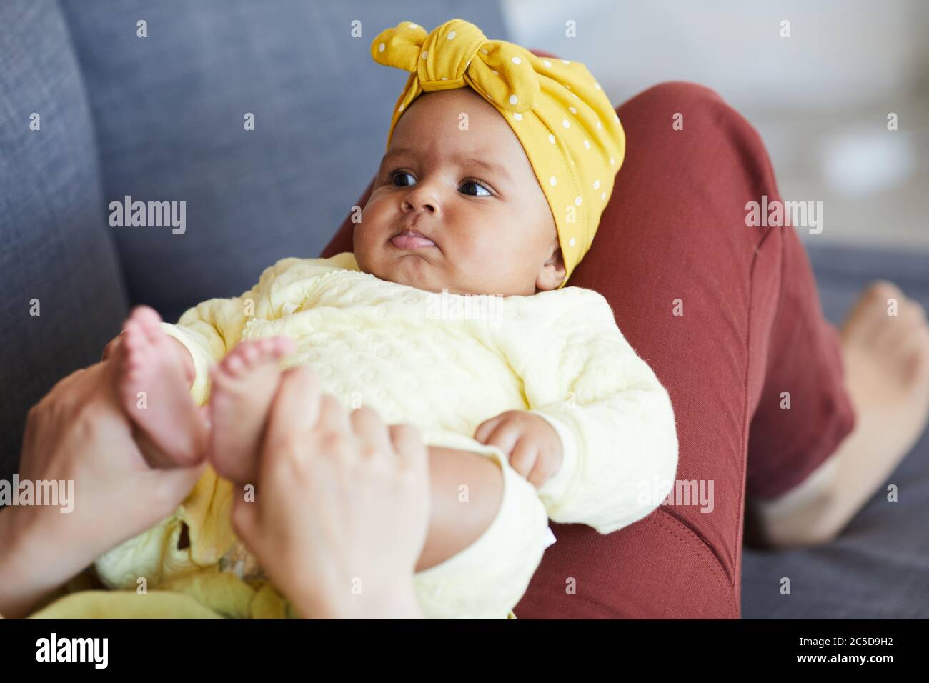 Beautiful baby girl lying on her mother's legs while they resting on sofa at home Stock Photo