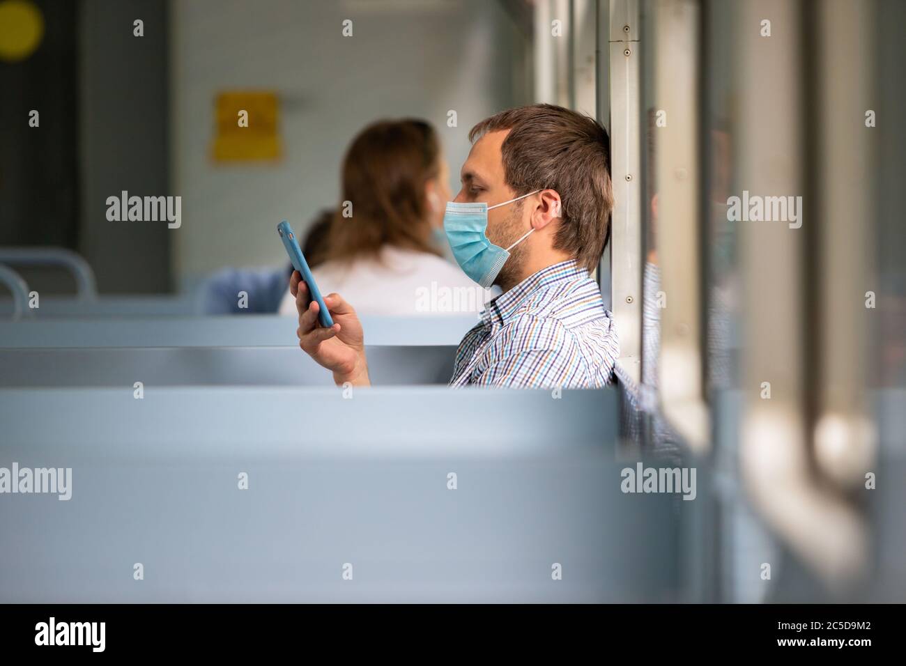 Man using smartphone, wears a protective mask in train to protect the respiratory system from coronavirus infection, covid-19. Preventive measure. New Stock Photo