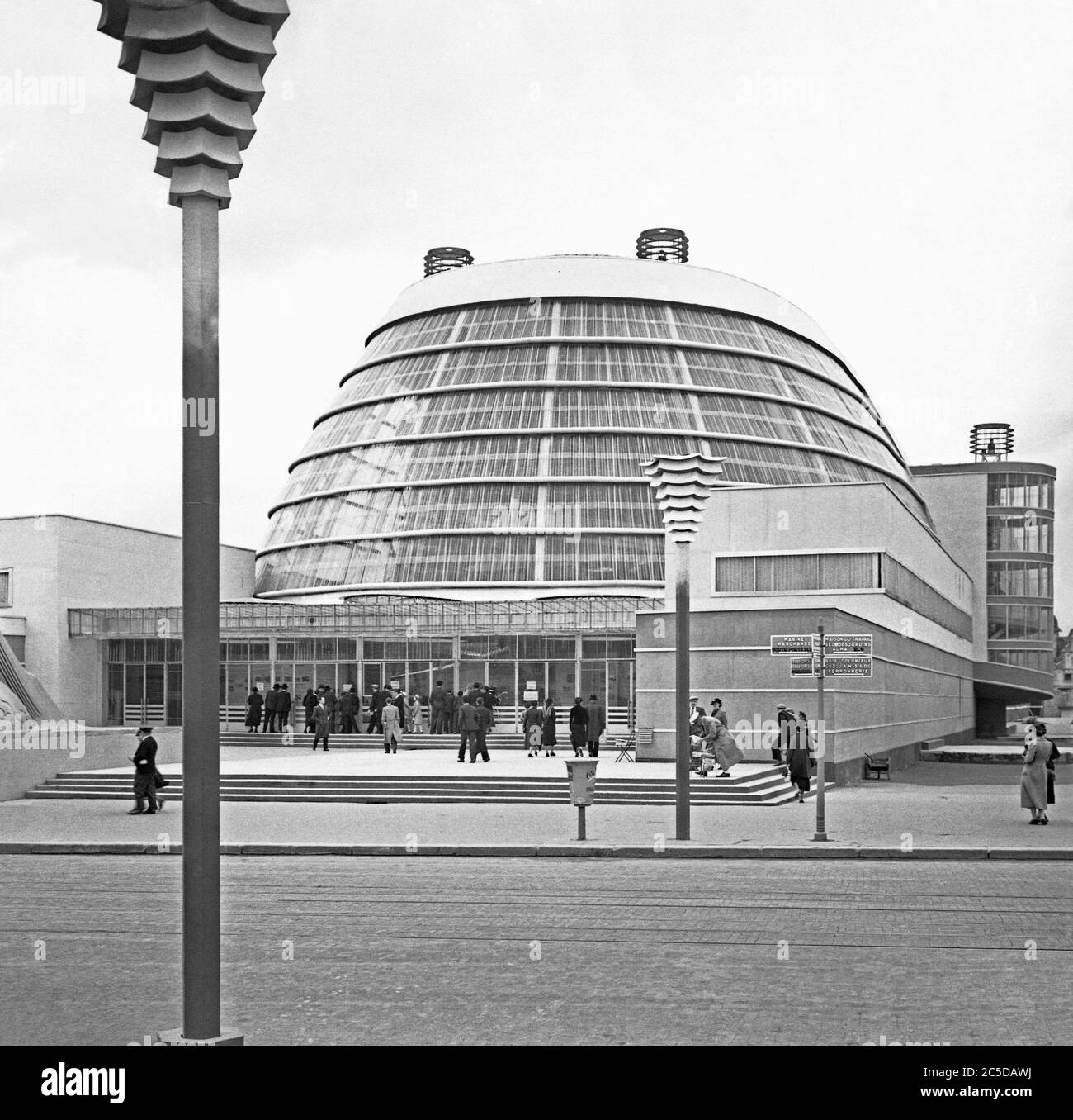 A view of the 1937 Expo (World's Fair or Exposition) held in Paris, France – here people in front of the Palais de l'Air (Palace of the Air), a striking modern building in the 'Sections Transports' part of the site. This pavilion was a large series of galleries designed by Audoul, Hartwig and Gérodias. Housing aviation displays, the centerpiece of the Air pavilion was the vast curved steel and glass gallery that echoed an aircraft hanger. Inside were giant aluminum rings, reminiscent of the rings of Saturn, encircled a plane in a display designed by Robert and Sonia Delaunay. Stock Photo