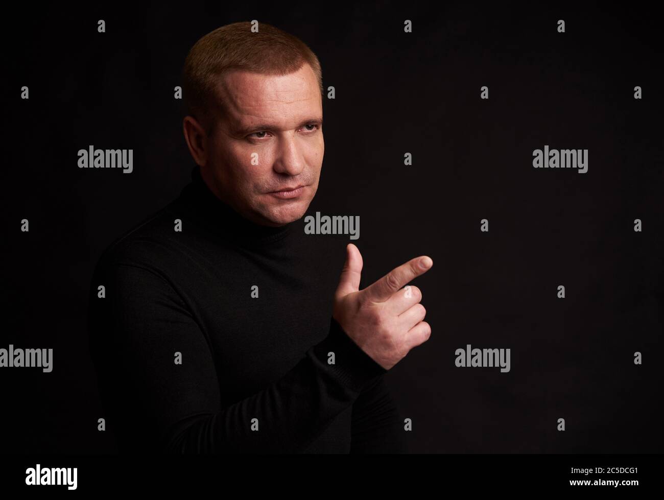 Serious man pointing finger looking away. Isolated on black background Stock Photo