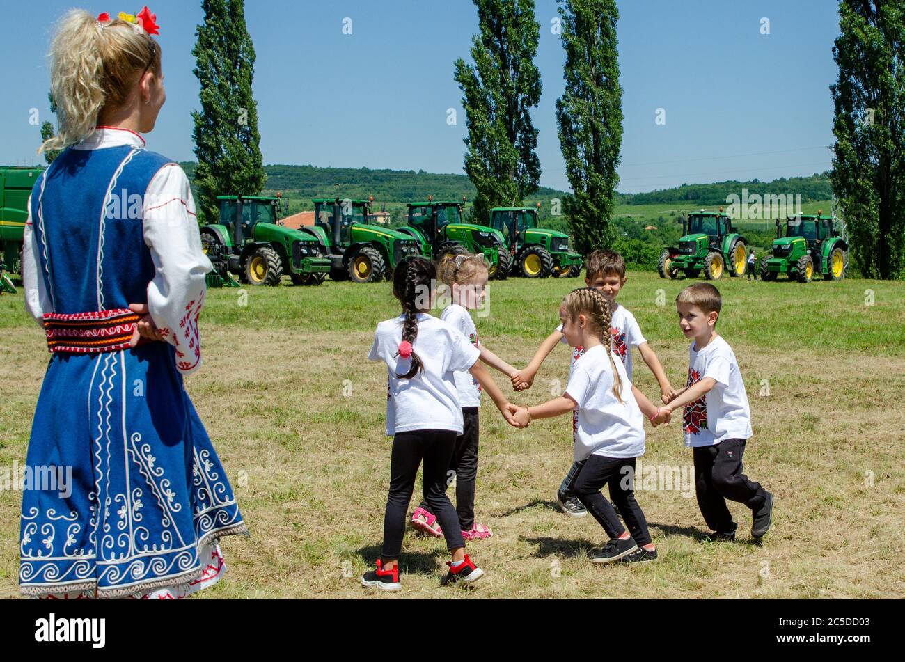 Bulgarian children dancing the horo to celebrate traditional custom of wheat harvest in countryside village. Stock Photo