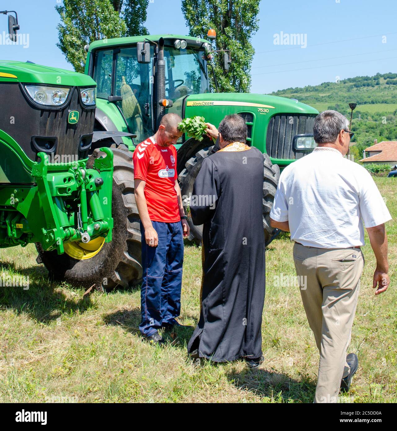 Bulgarian priest blesses local farm workers and farm machinery at traditional cultural wheat harvest festival Stock Photo