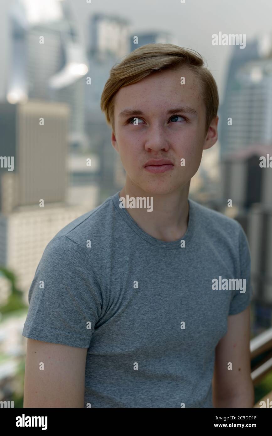 Young handsome blond teenage boy thinking against view of the city ...