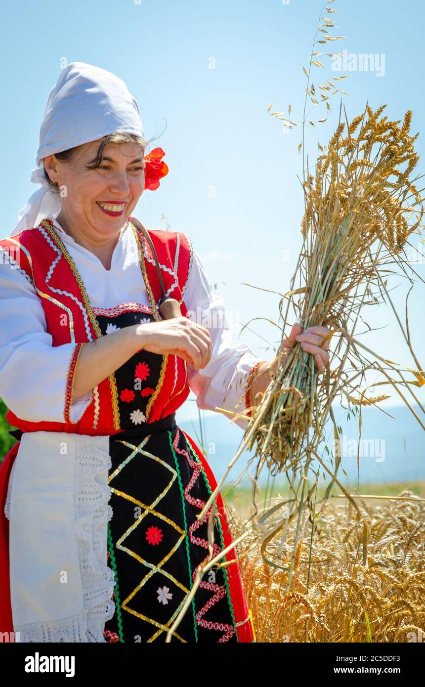Bulgarian woman in field with wheat sheaf celebrate traditional custom of wheat harvest in countryside village. Stock Photo