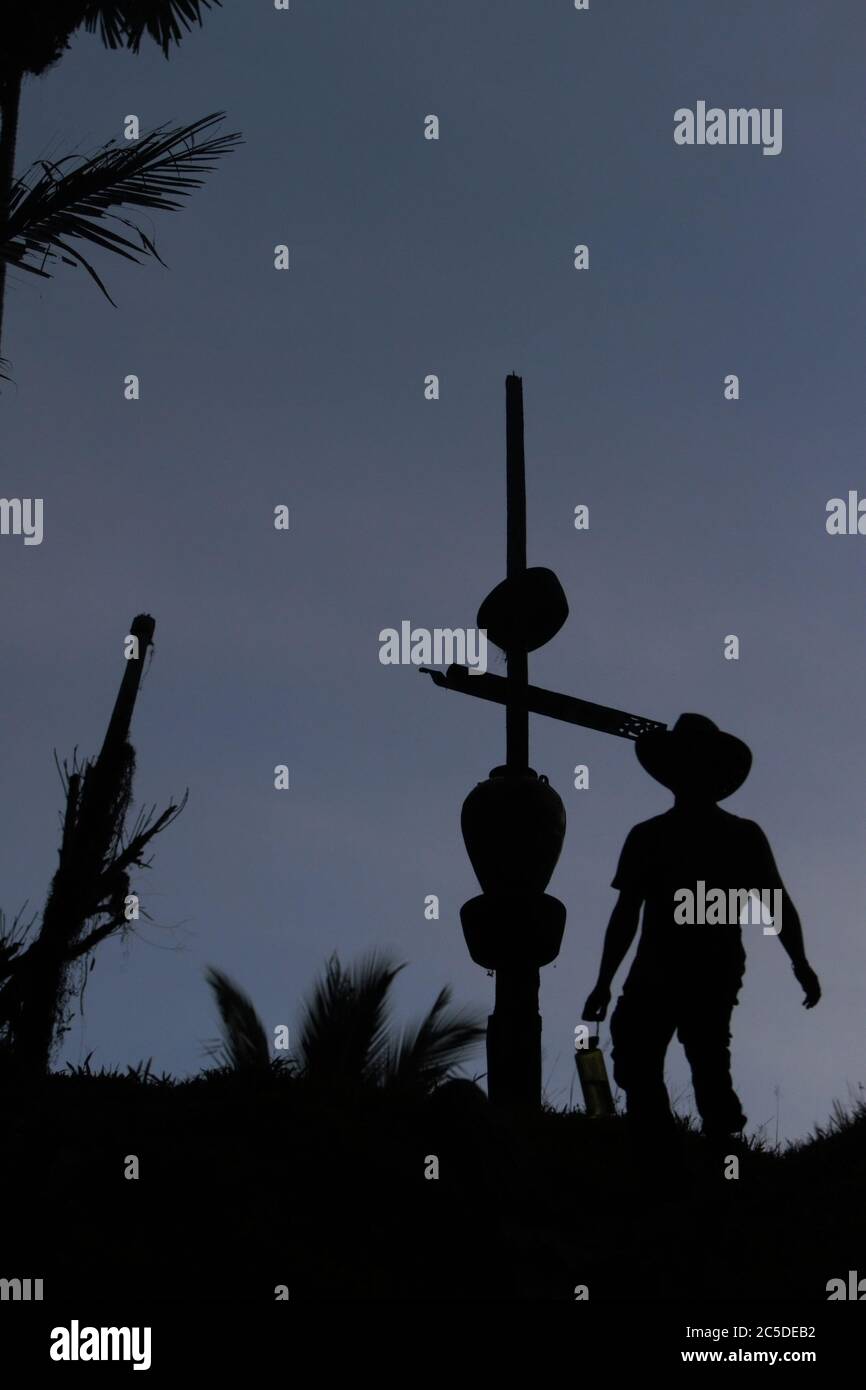 A facilitator of community-based ecotourism assessment wearing cowboy hat is silhouetted against bright sky as he is walking past a totem pole on the bank of Manday river in remote village of Nanga Raun in Kalis, Kapuas Hulu, West Kalimantan, Indonesia. 'The pole is a sign of the settlement area in the village, as well as a symbol to greet ancestor spirits,' said an elder in the village that is mostly inhabited by the indigenous Orung Da'an Dayak community. Stock Photo