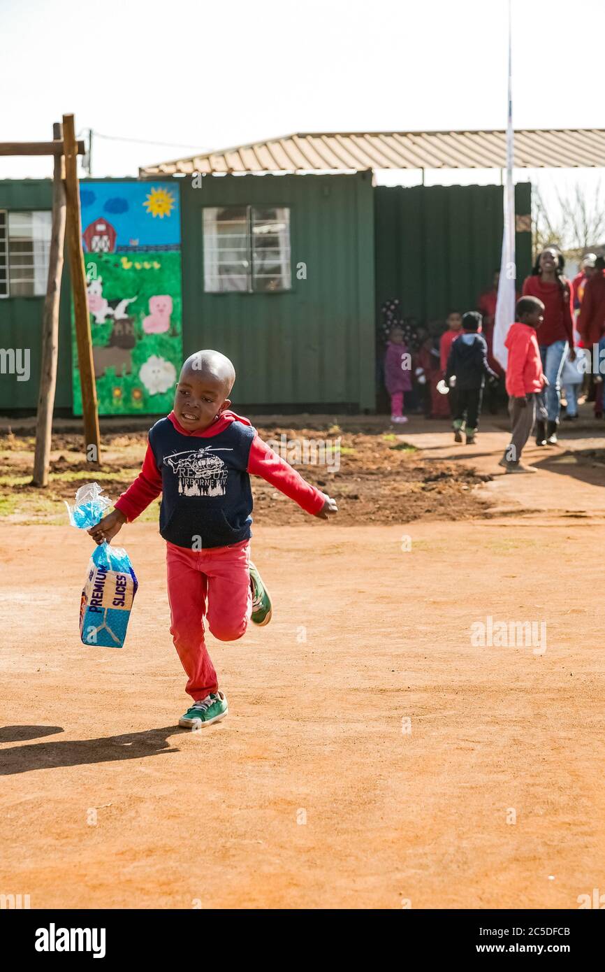 Soweto, South Africa - July 18, 2016: Young African Preschool kids running with a loaf of bread in the playground of a kindergarten school Stock Photo