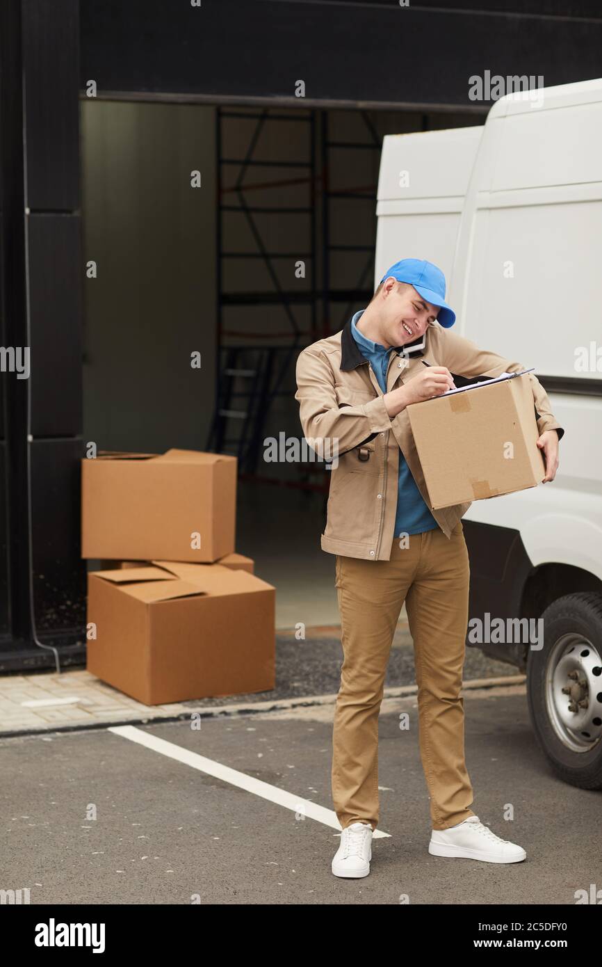 Young man talking on mobile phone while working with load in warehouse Stock Photo