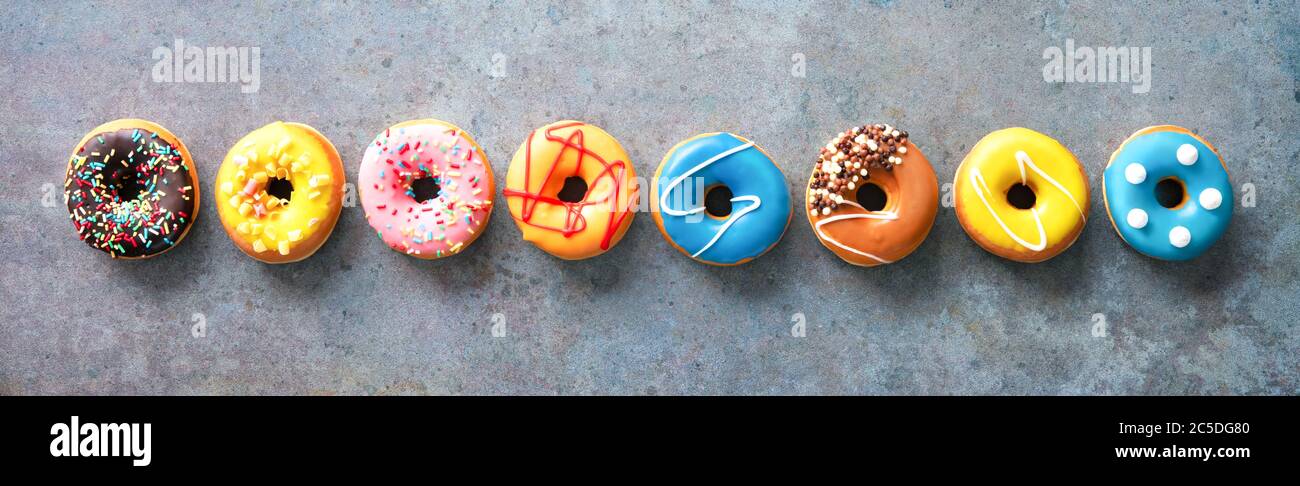 Various colourful donuts in a row on rustical grey background Stock Photo