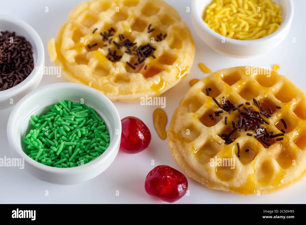 Mini waffles, cake sprinkles and cherries on white background syrupy