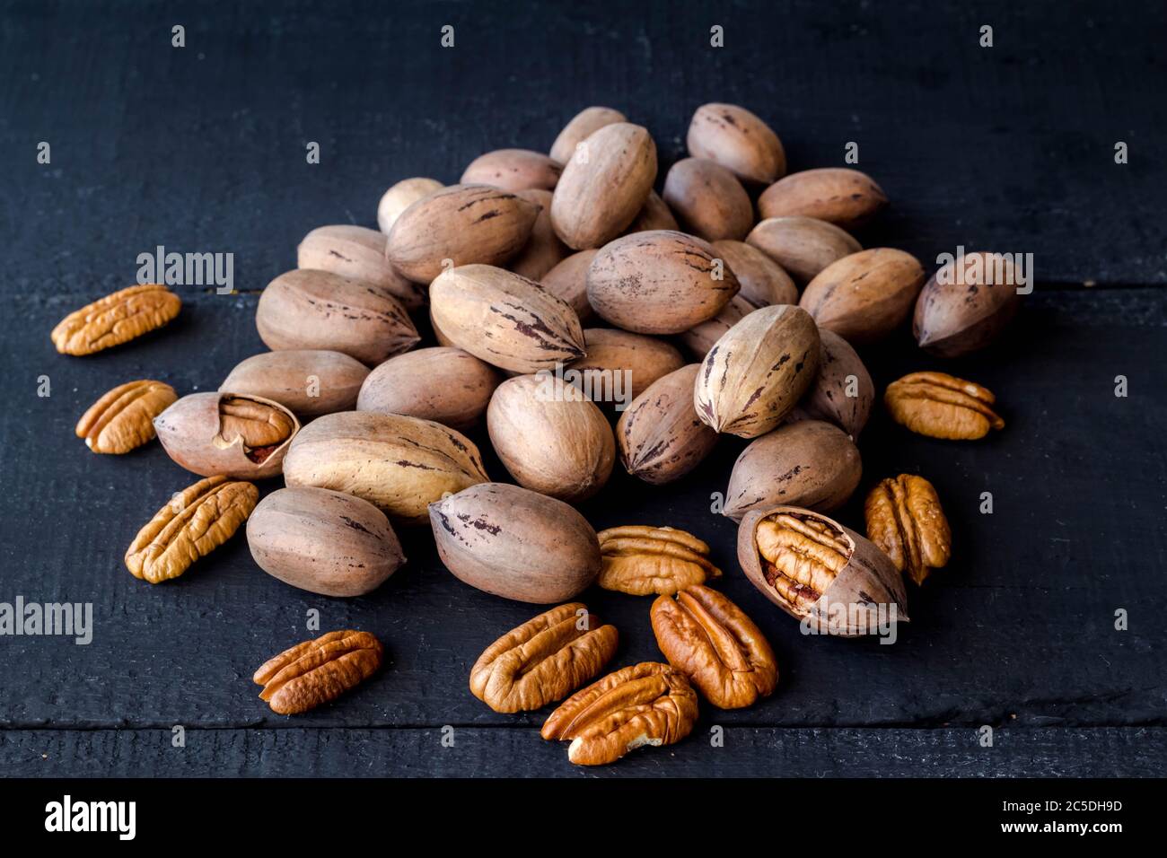 Pecan nuts in shell, cracked and halves isolated on rustic black wooden plank background Stock Photo