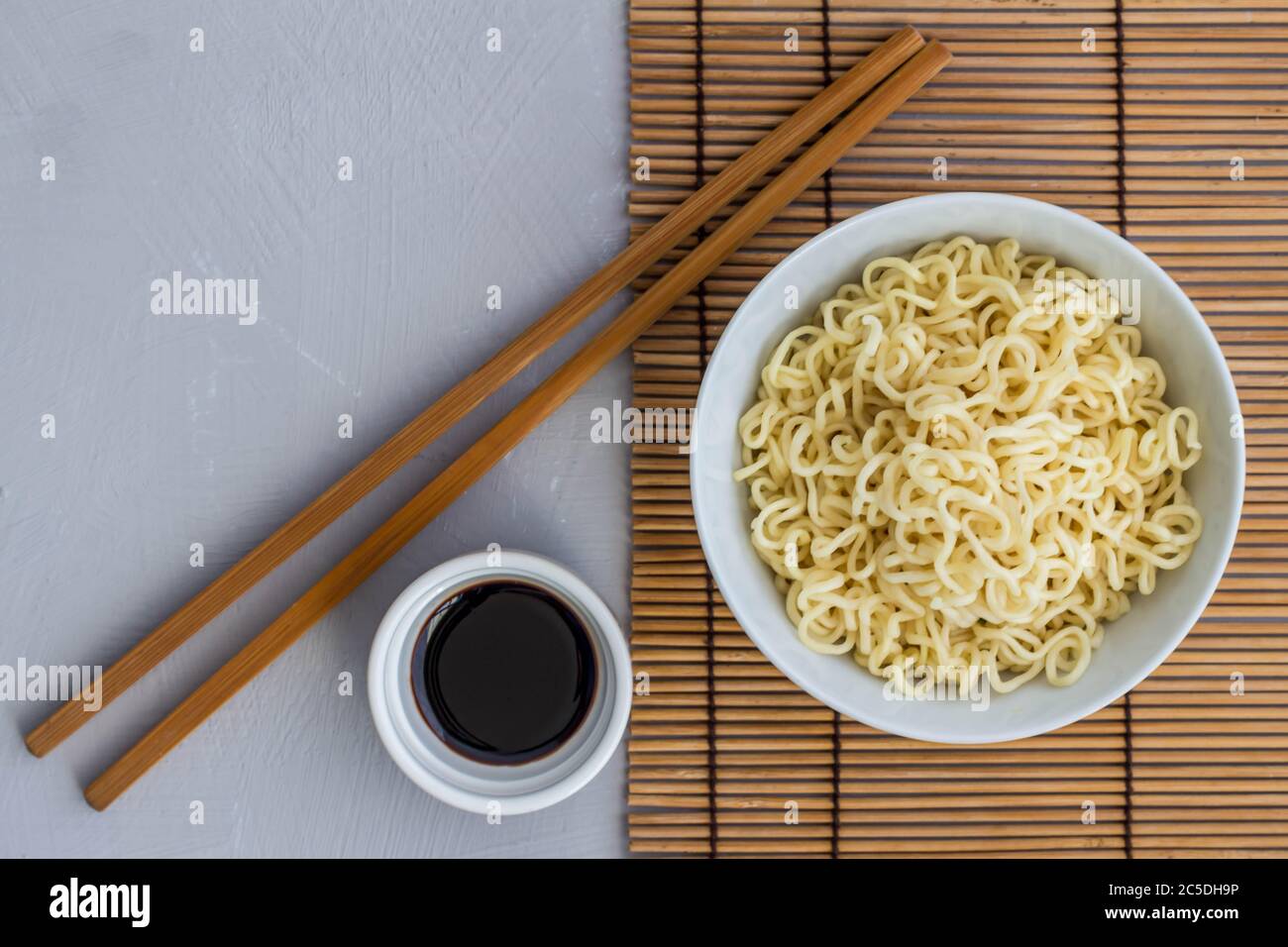 Bowl of plain cooked noodles with chopsticks and little bowl of soy sauce - overhead view photo with text space Stock Photo