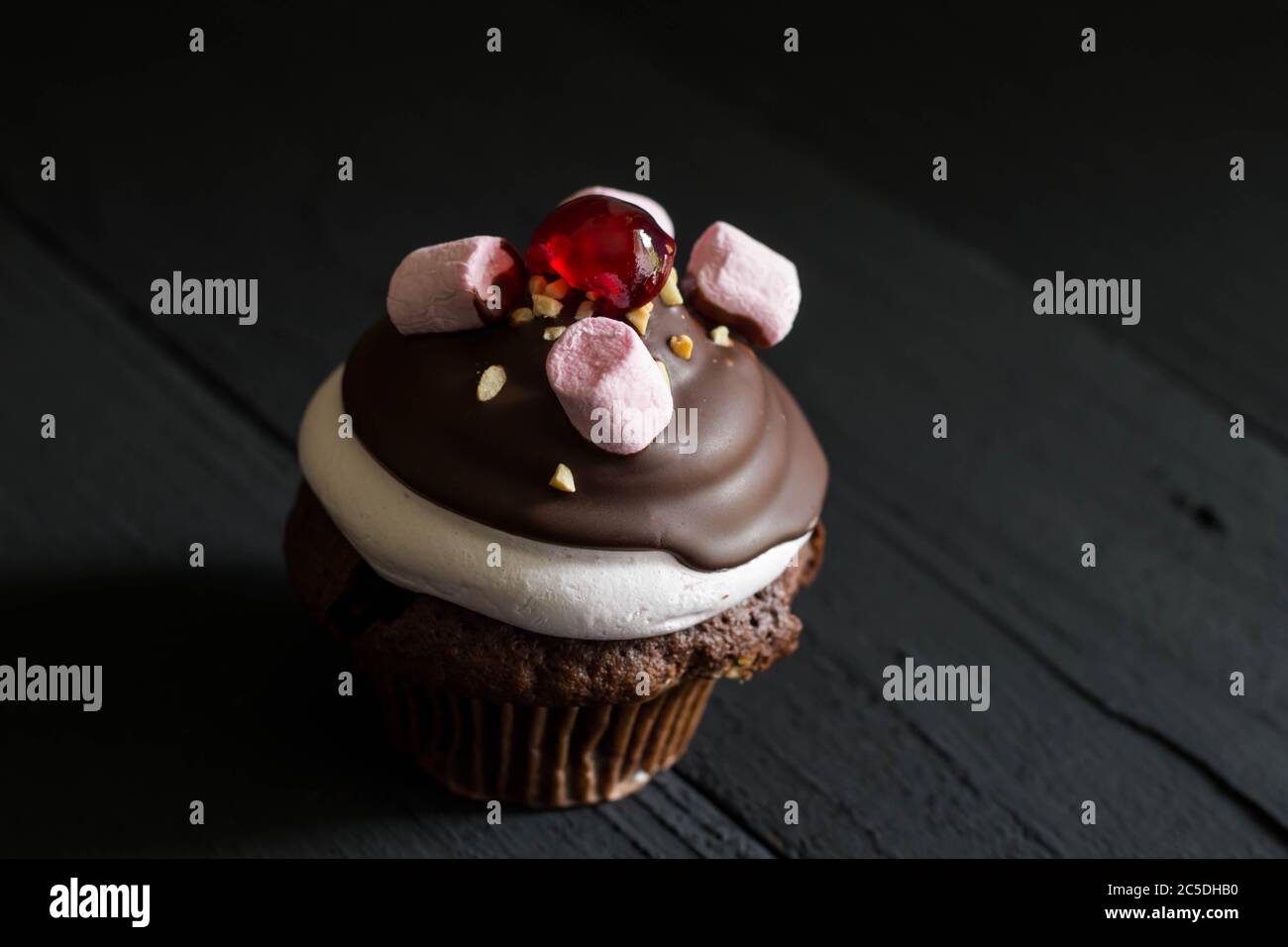 Decadent marshmallow and chocolate coated cupcake isolated on black rustic background with space for text Stock Photo