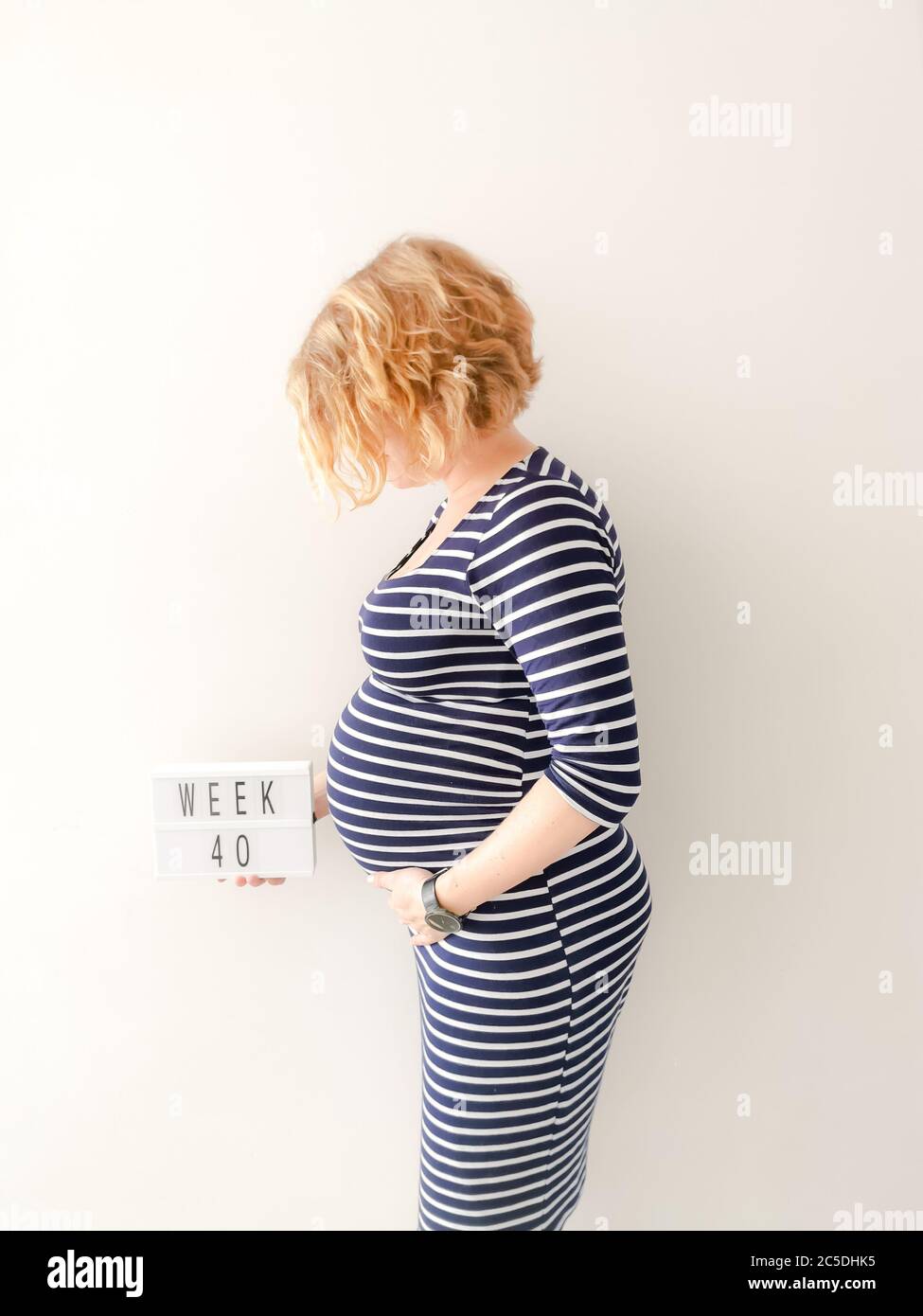 Pregnant young caucasian female touching her growing belly and holding a sign with 40 weeks Stock Photo