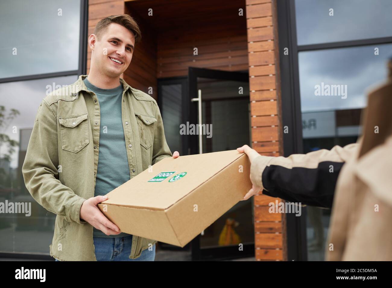 Young smiling man getting the parcel from postman while they standing outdoors Stock Photo