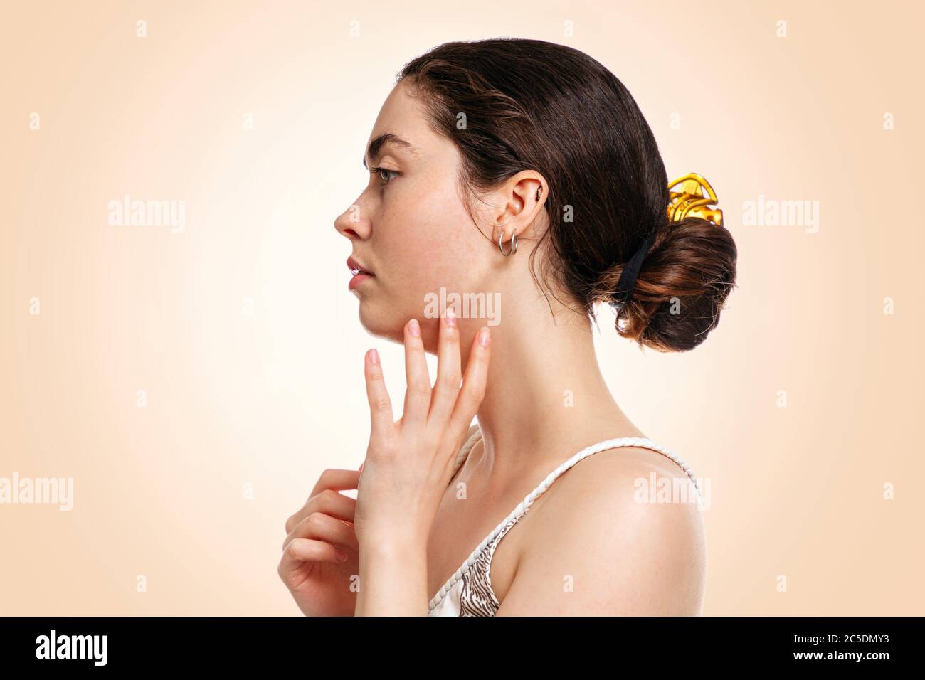 A young beautiful woman holds her hand to her face.Side view. Beige background. Copy space.Concept of rejuvenation, beauty and cosmetology. Stock Photo