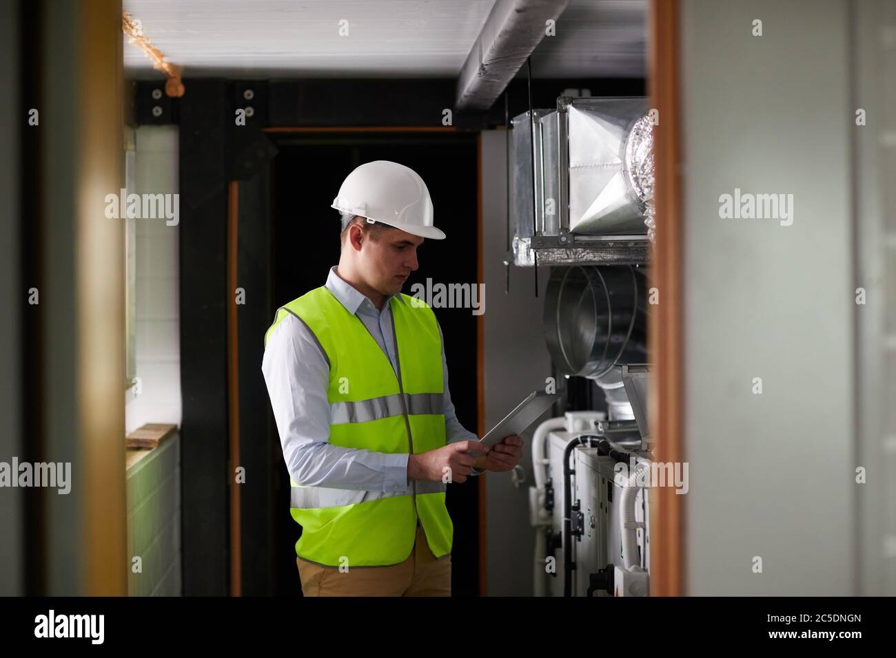 Young engineer in work helmet using digital tablet while working in the factory Stock Photo