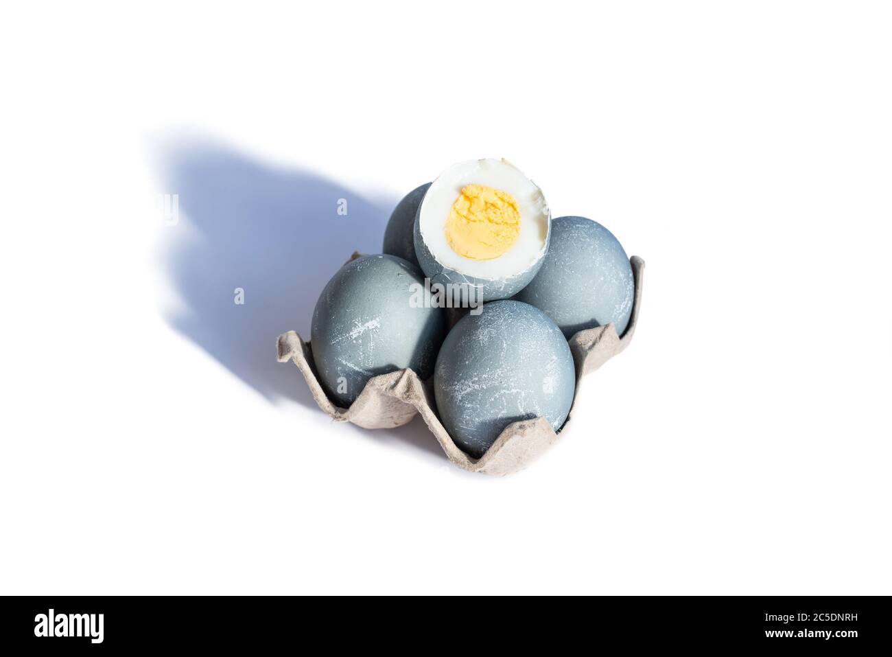 Four easter eggs in color of concrete in cardboard tray and one boiled egg is cut on white background. Happy Easter concept. Copy space Stock Photo