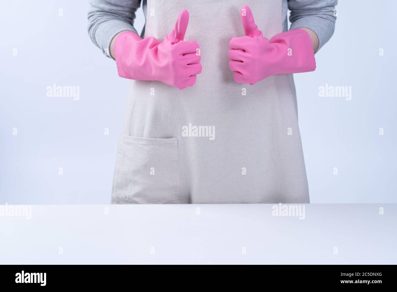Young woman housekeeper in apron is wearing pink gloves to clean the